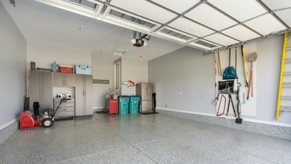 Clean residential garage interior with an open garage door, wall-mounted tools, storage cabinets, and epoxy floor